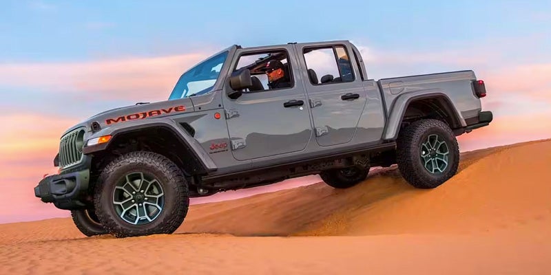 Dark gray Jeep Gladiator driving over a sand dune