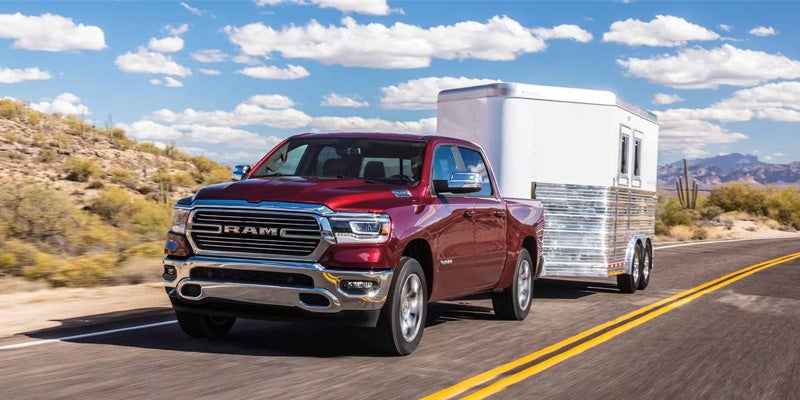 A red RAM 1500 pickup truck towing a large camping trailer down a stretch of desert highway backed by scrubgrass and blue skies.