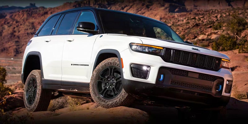 A white Jeep Grand Cherokee sitting atop a bluff, showing the dirt from its trailblazing capabilities