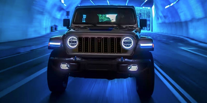 An image of a fierce-looking Jeep Wrangler facing the camera, its headlights on with a dark blue background.