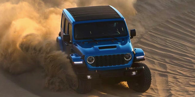 A blue Wrangler tearing up a sand dune as it tackles difficult terrain.